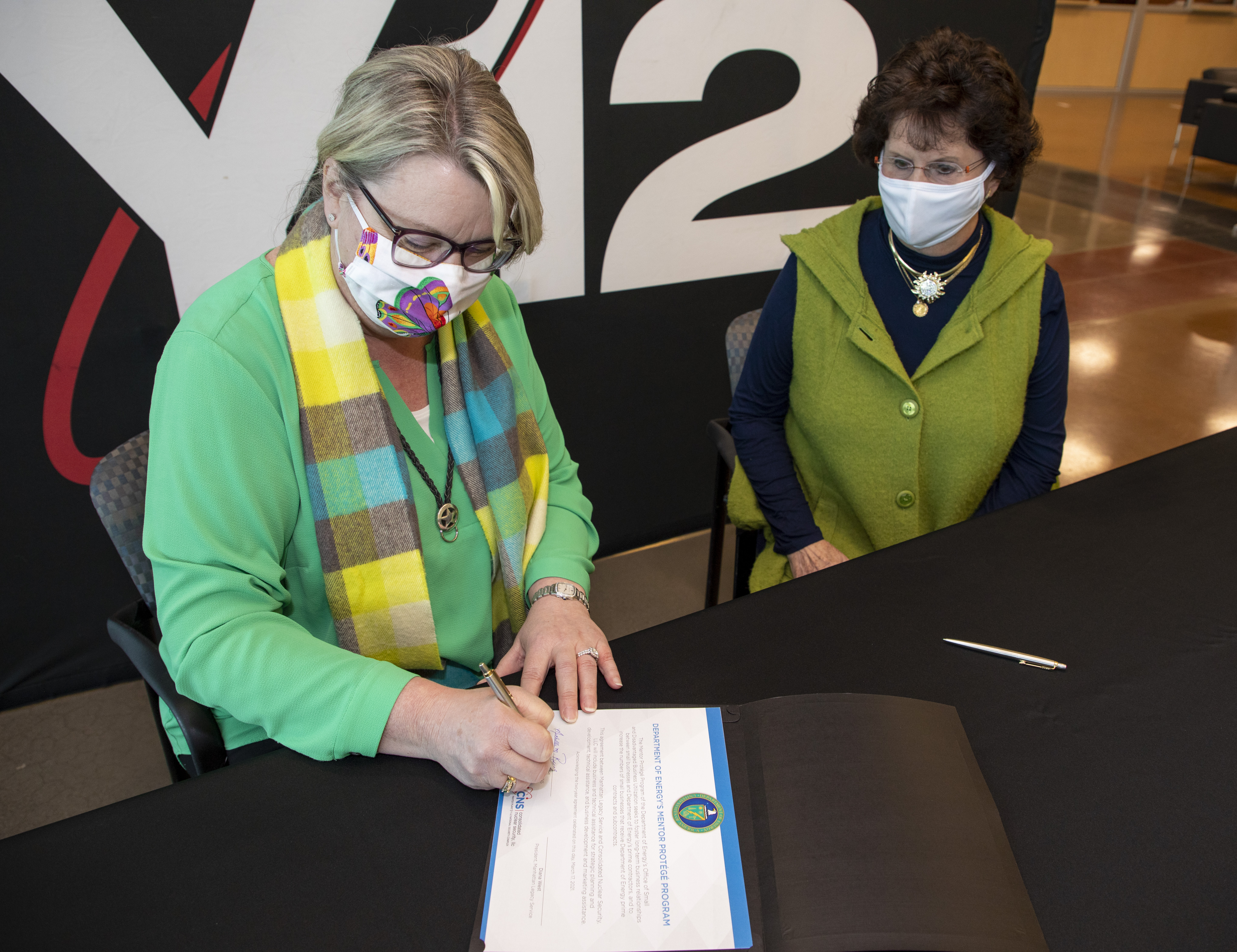Consolidated Nuclear Security President and CEO Michelle Reichert signs the Mentor-Protégé Agreement with Manhattan Legacy Services as Diana West, president and founder of Manhattan Legacy Service, observes.  