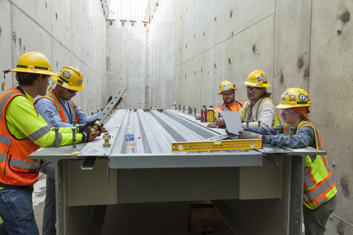 A Uranium Processing Facility team meeting is held in a Main Process Building corridor. 