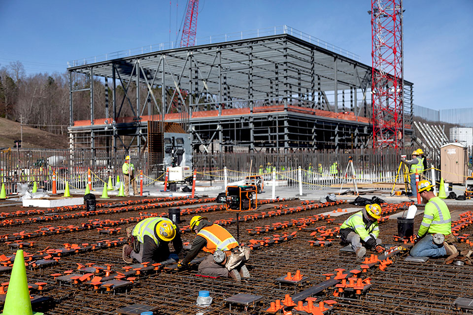 Workers placing embed plates for UPF’s Salvage and Accountability Building. The Mechanical Electrical Building is in the background.