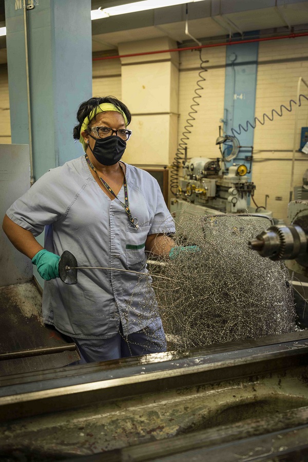 Laura Dye, machine cleaner, removes chips from a lathe.