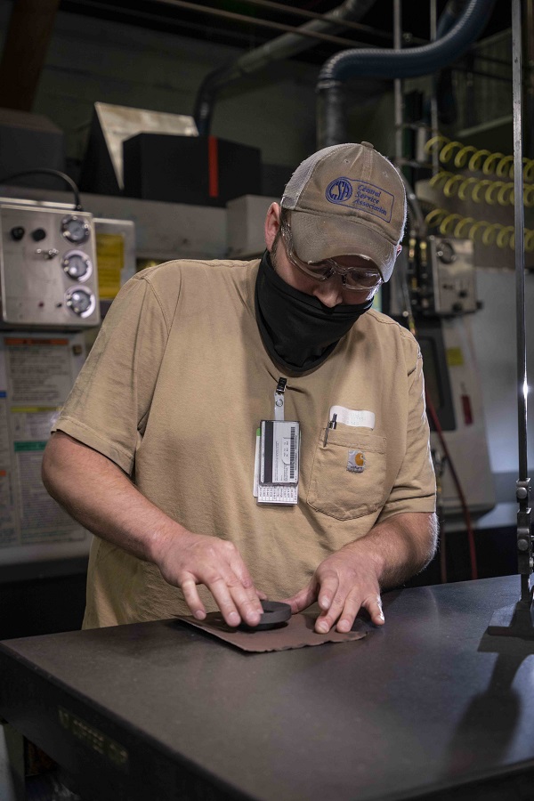 Machinist Justin Acres sands a graphite part flat on a surface plate.