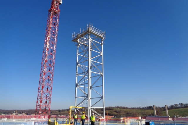 UPF employees stand on the roof of the Salvage and Accountability Building in front of the process off gas stack.