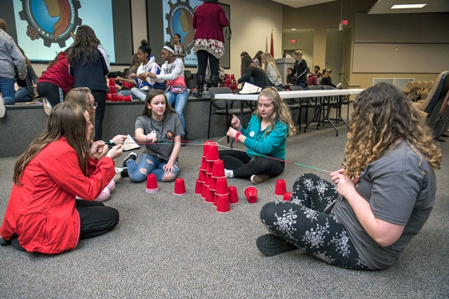 Introduce a Girl to Engineering participants work as a team to build a tower using a rubber band to pick up cups and place them on top of each other by pulling and releasing strings on the rubber band.